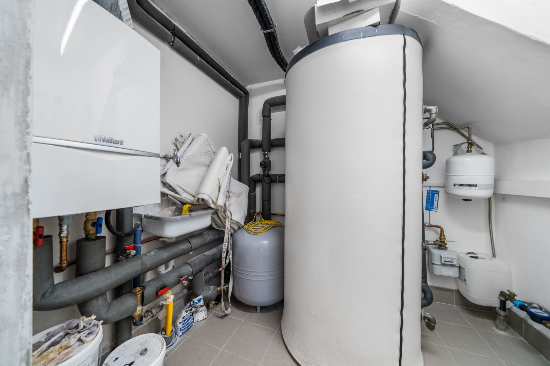 Technikraum mit großem Warmwasserspeicher, Rohren, Heizungsanlage und verschiedenen Geräten.