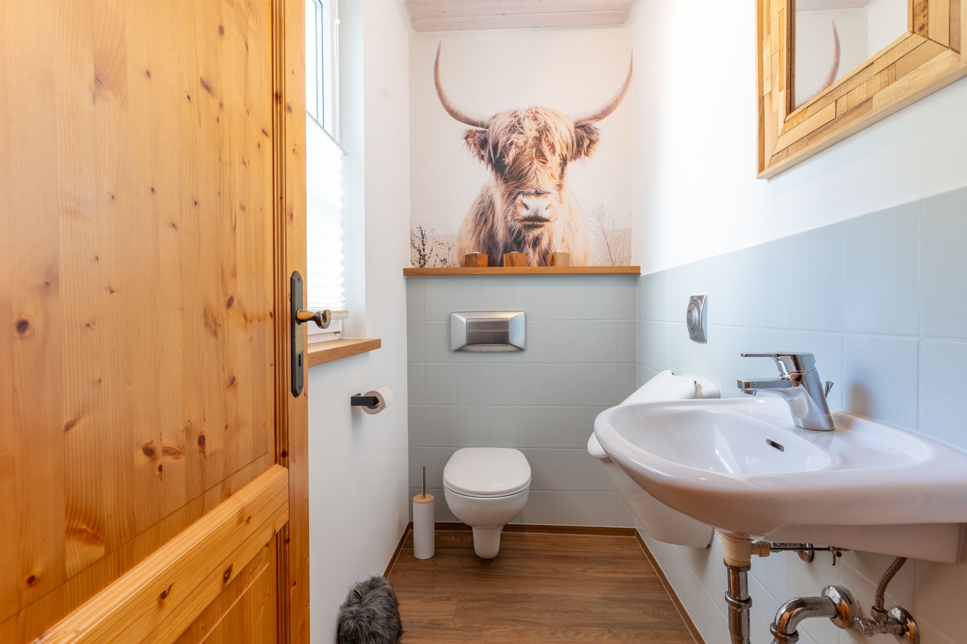 Kleines Badezimmer mit WC, Waschbecken und Bild eines Hochlandrinds an der Wand.