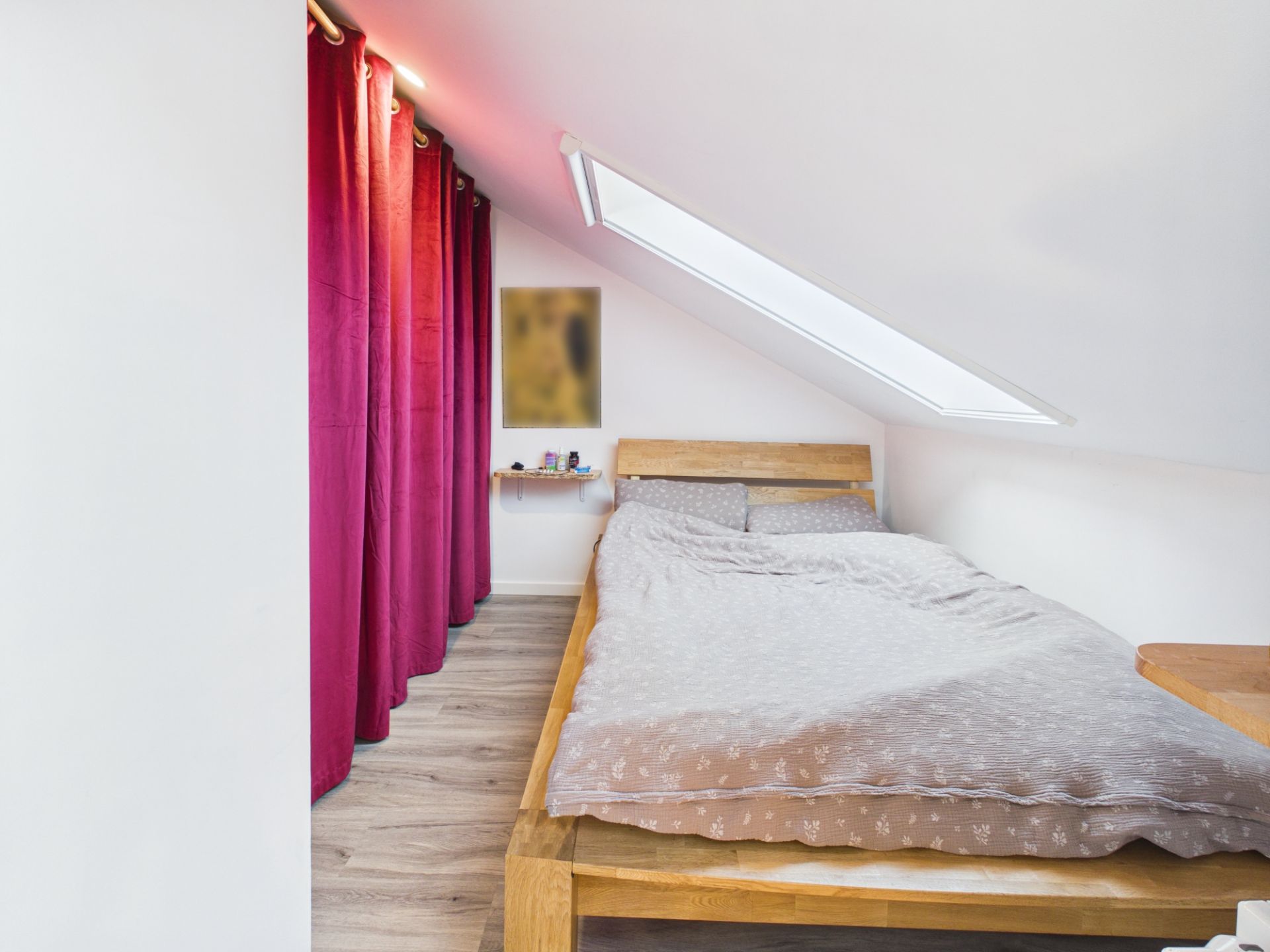 Schlafzimmer mit Dachschräge, Holzbett, Dachfenster und roten Vorhängen.