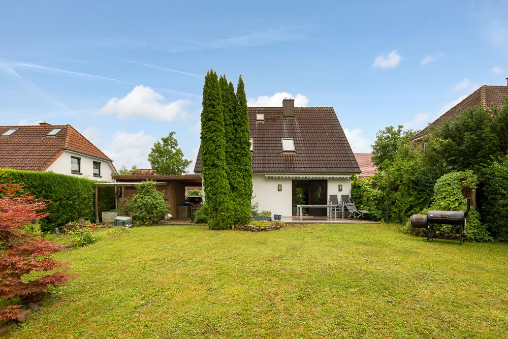 Garten mit Rasen, Sträuchern und kleinem Einfamilienhaus im Hintergrund.
