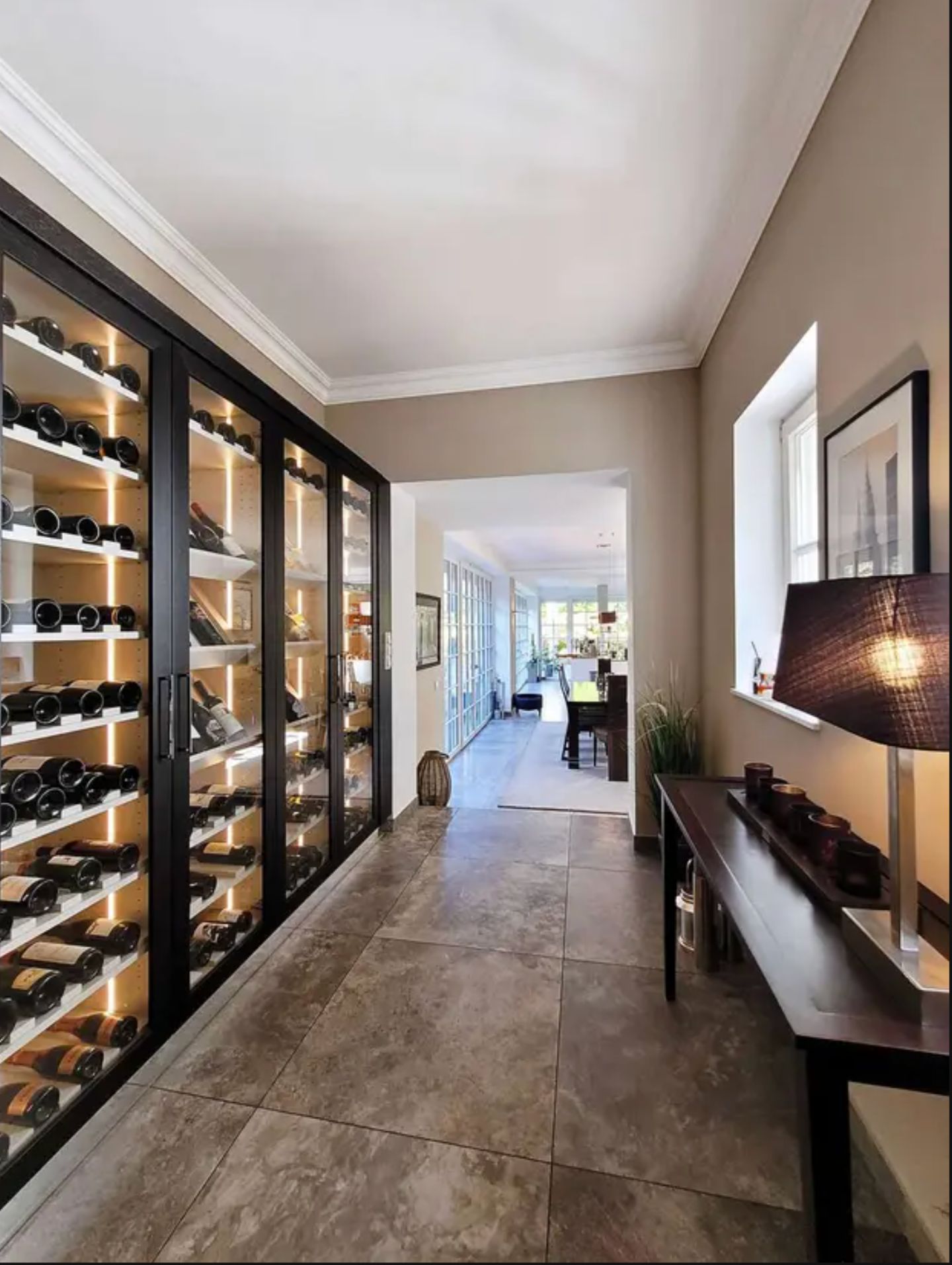 Flur mit beleuchtetem Weinschrank, Beistelltisch und Blick ins Esszimmer.