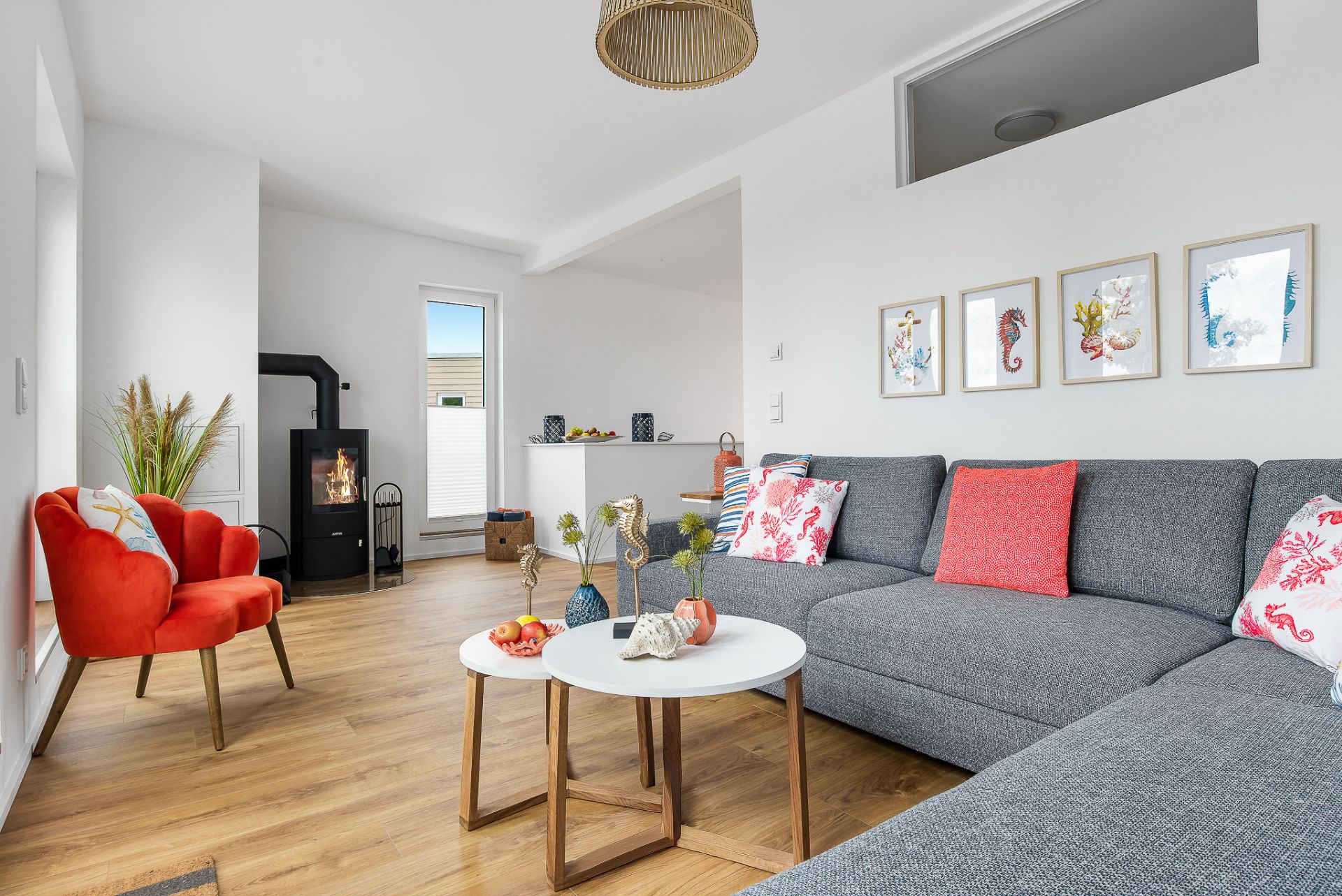 Helles Wohnzimmer mit grauem Sofa, rotem Sessel, Kamin und kleinem Couchtisch auf Holzfußboden.