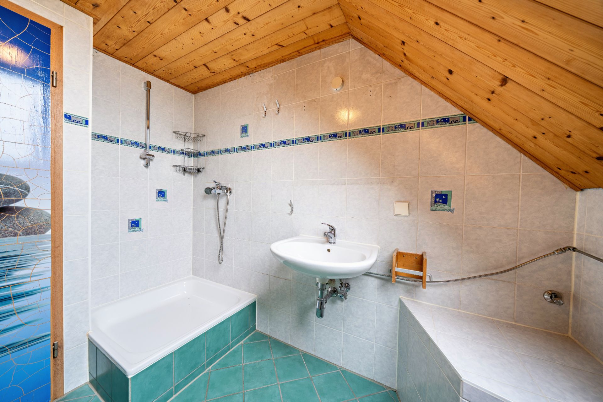 Badezimmer mit Dusche, Waschbecken und Holzdecke unter einer Dachschräge.