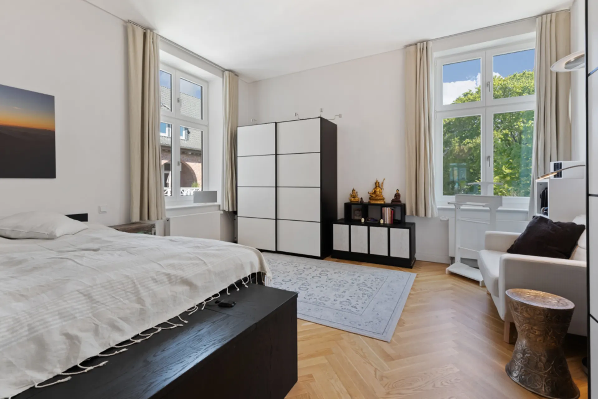 Helles Schlafzimmer mit großem Bett, weißen Schränken, Teppich und großen Fenstern mit Vorhängen.