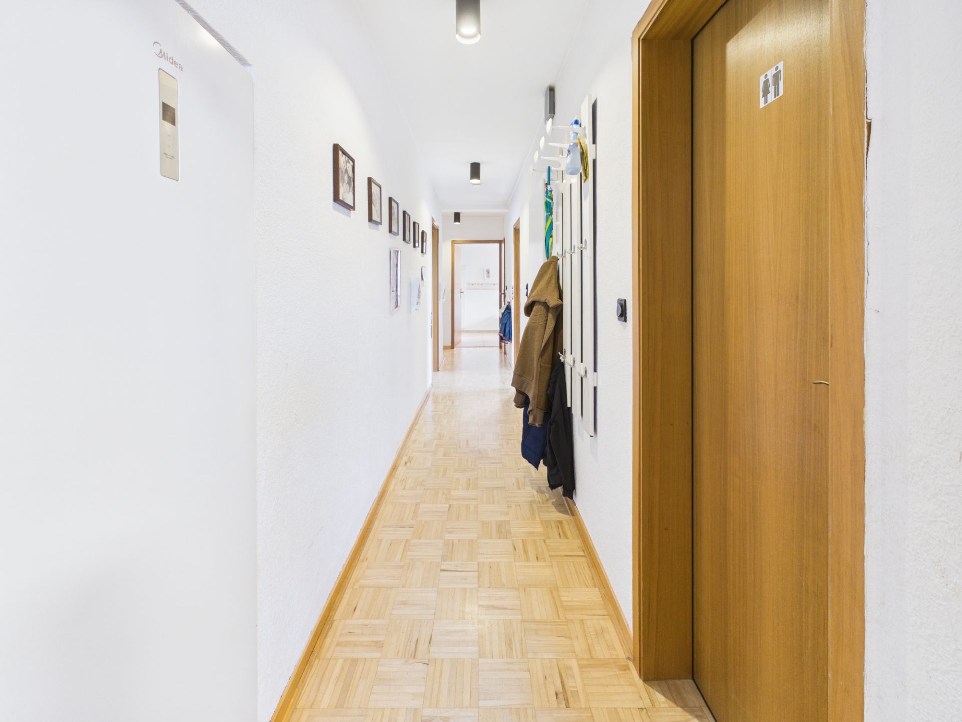 Heller Flur mit Holzboden, Türen und Garderobe, Bilder an der weißen Wand.