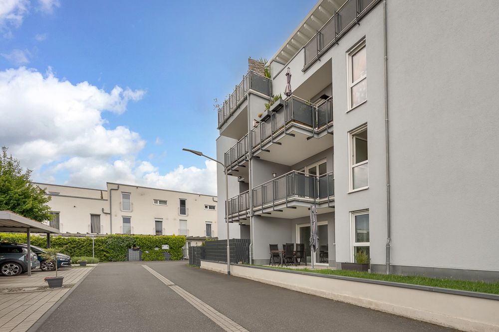 Modernes Wohnhaus mit mehreren Balkonen und Parkplätzen im Vordergrund.