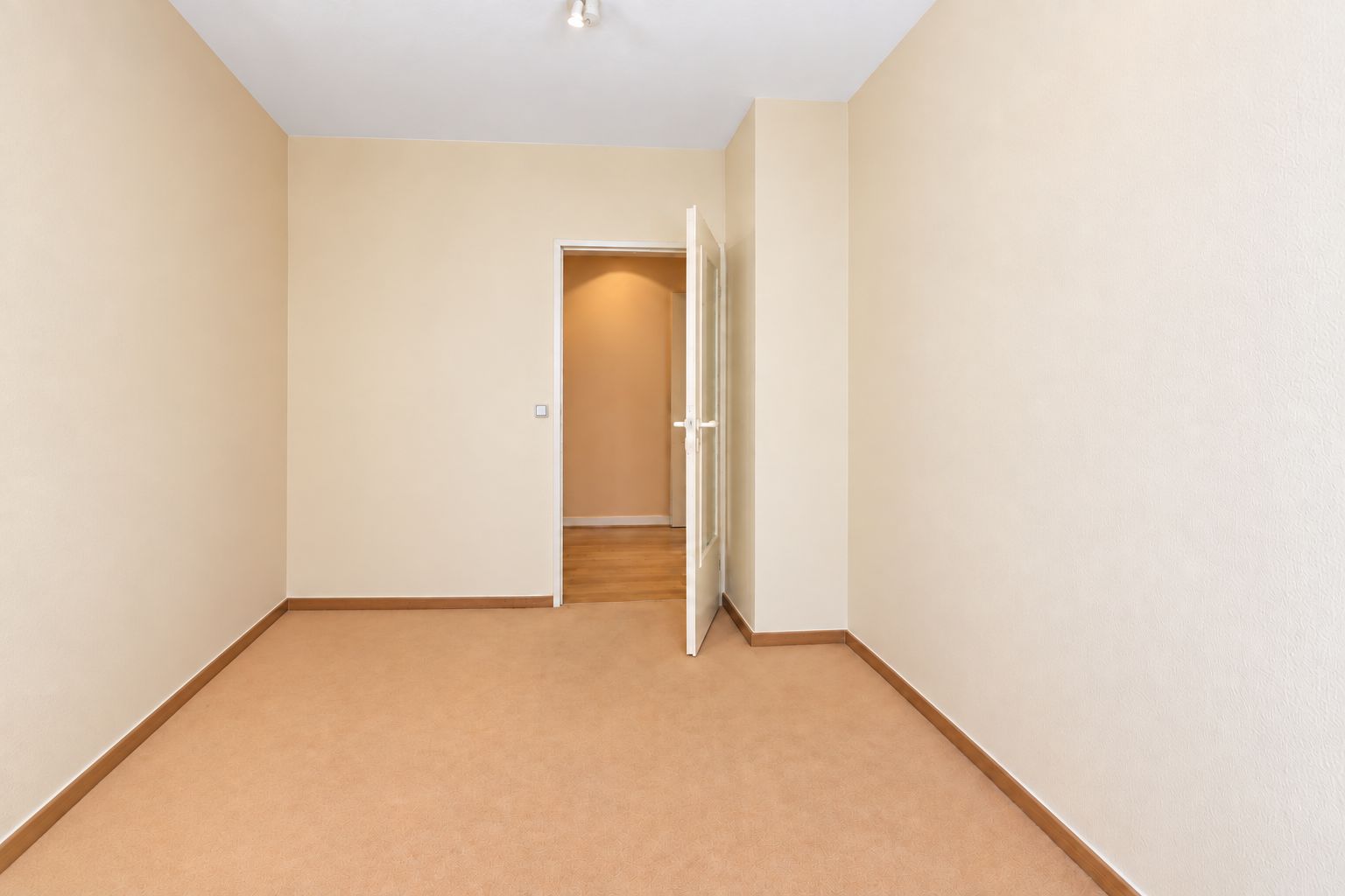Leerer Raum mit beigen Wänden, Teppichboden und geöffneter Tür.