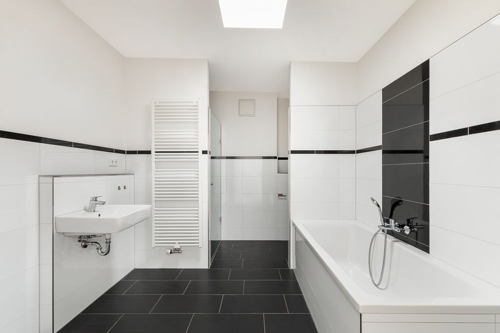 Modernes Bad mit weißem Waschbecken, Badewanne und schwarzen Fliesen.