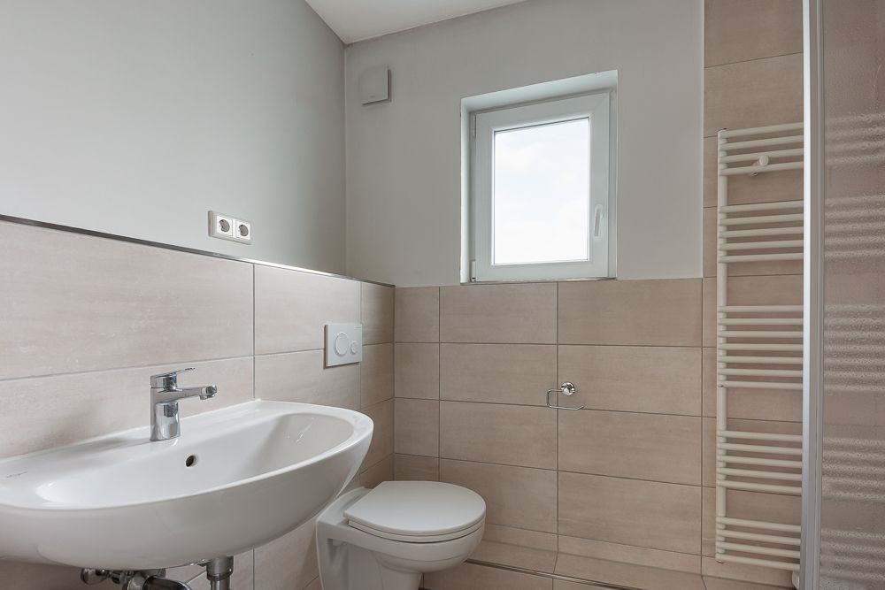 Modernes Badezimmer mit Waschbecken, Toilette, Fenster und Handtuchheizkörper.