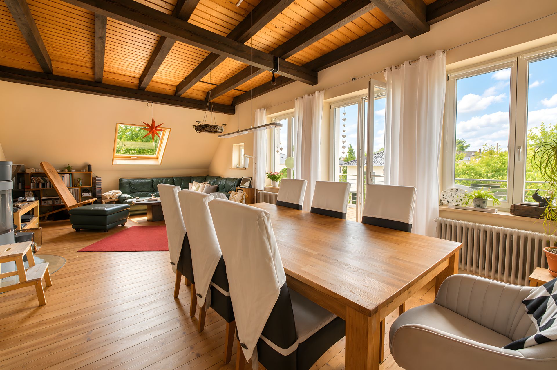 Helles Wohnzimmer mit Essbereich, Holztisch, Stühlen und großer Fensterfront mit Blick ins Grüne.