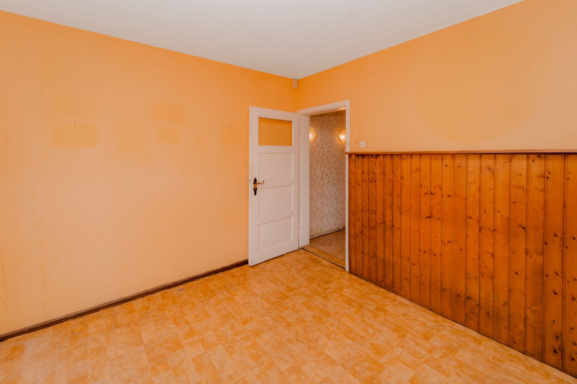 Leerer Raum mit oranger Wand, teils Holzverkleidung und offener weißer Tür.