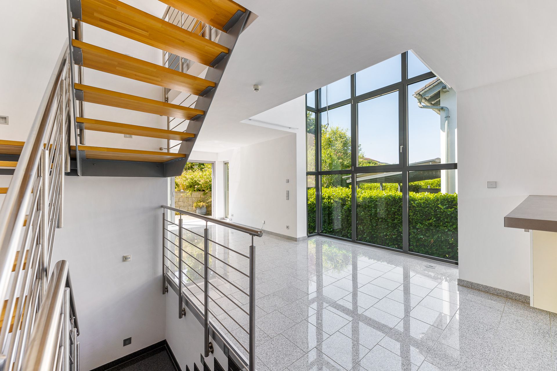 Helles Wohnzimmer mit großer Fensterfront und moderner Holztreppe.