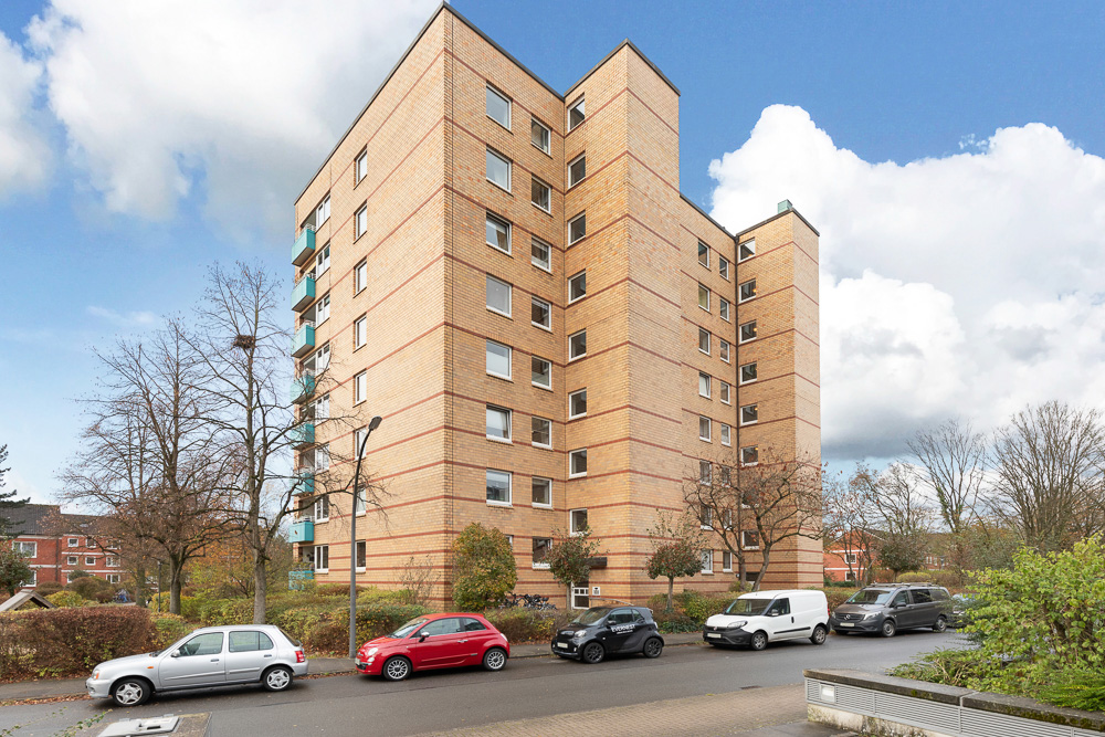 Mehrstöckiges Wohnhaus aus Backstein mit parkenden Autos davor.