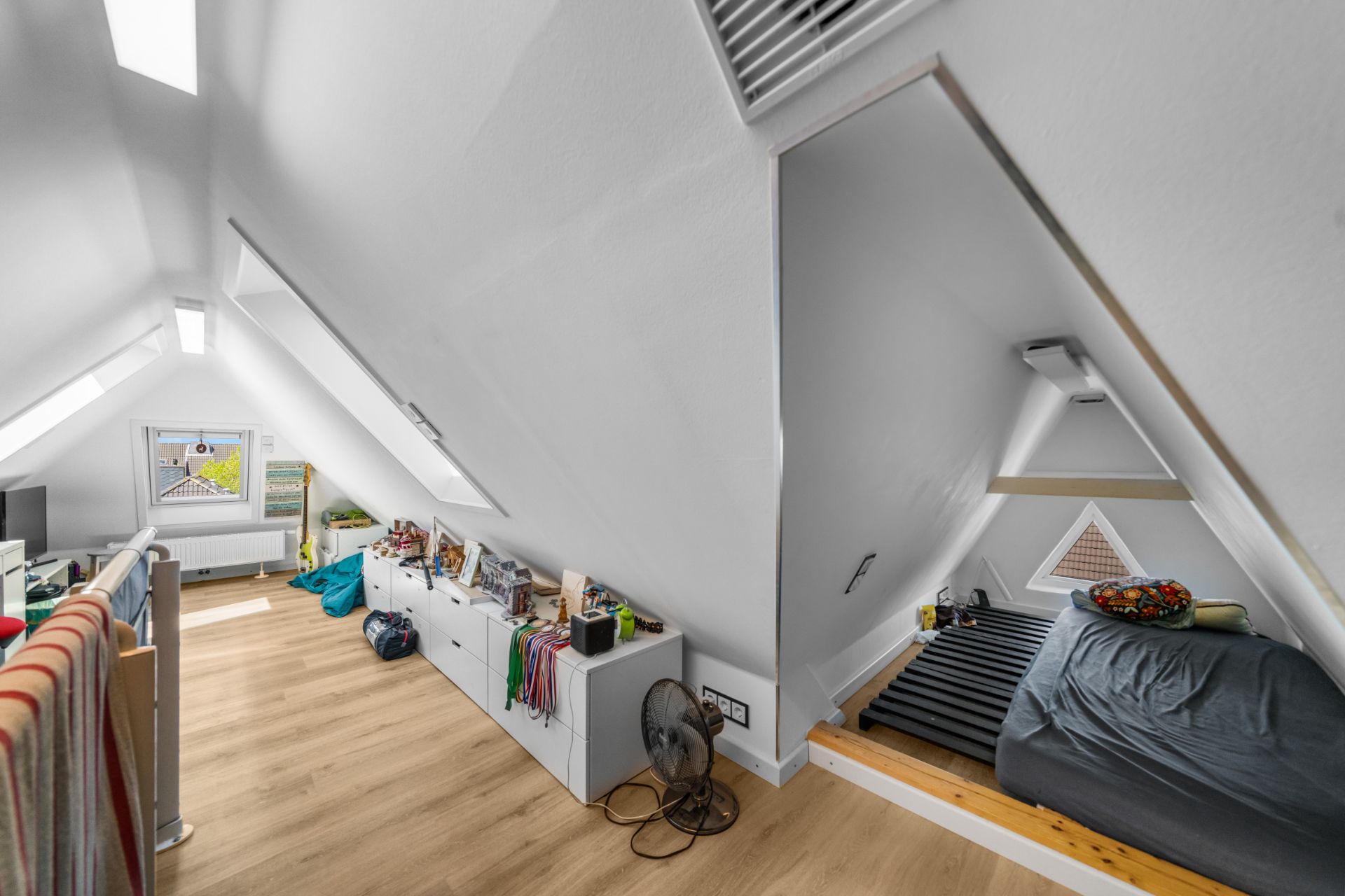 Helles Dachgeschosszimmer mit Holzfußboden, Bettnische und Stauraum unter Dachschrägen.