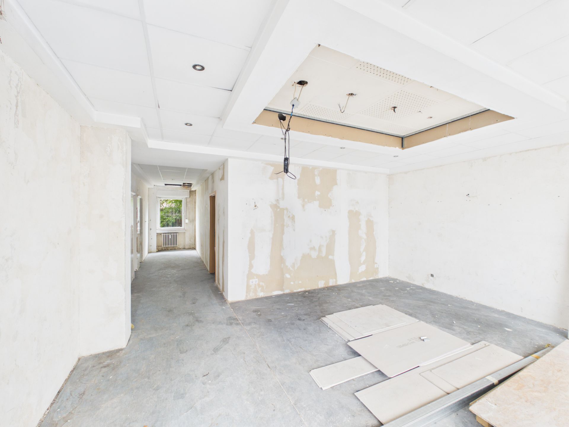Leerer Raum mit abblätternden Wänden, grauem Boden und losem Baumaterial auf dem Boden.