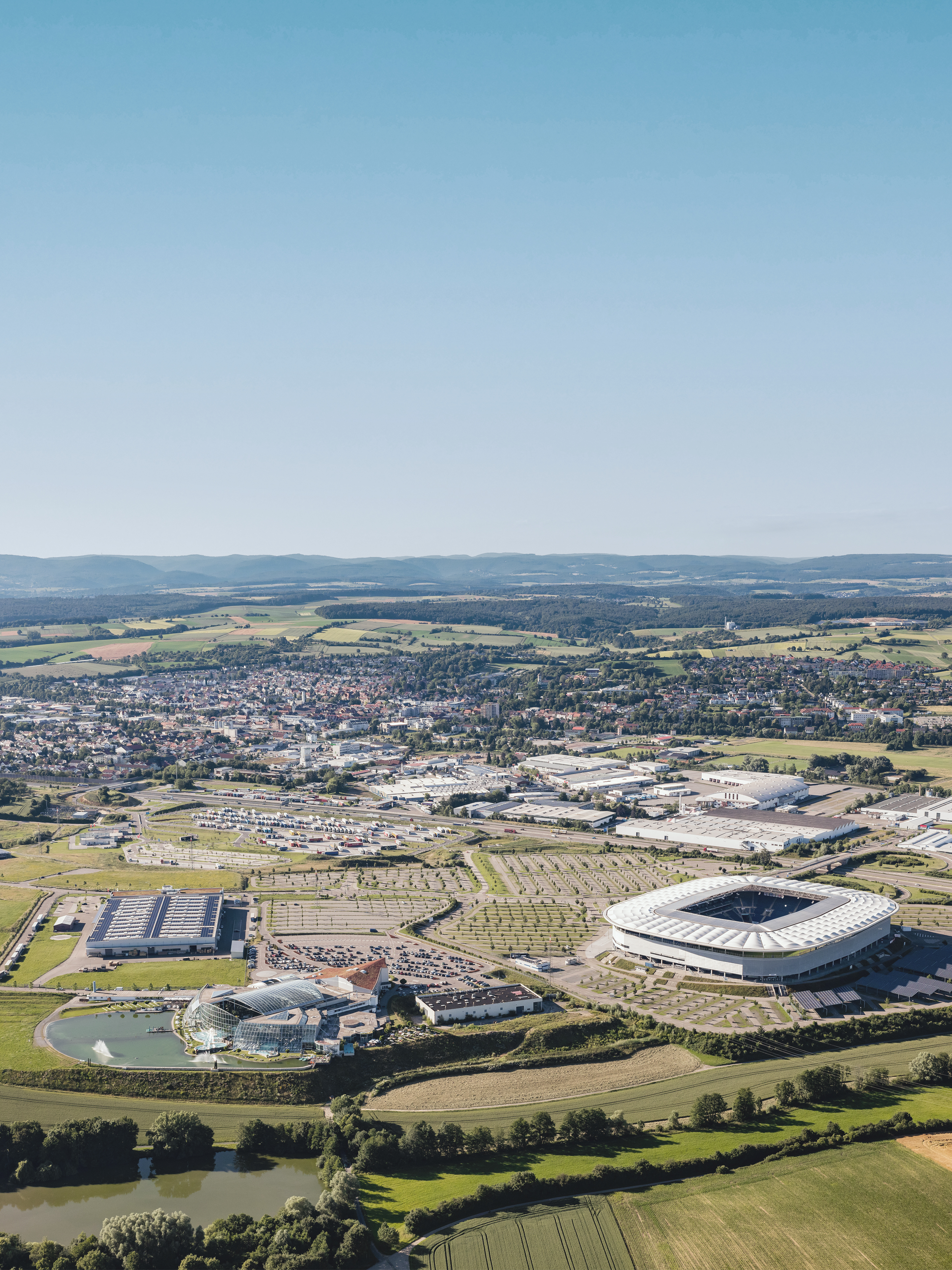 Luftaufnahme einer Stadt mit Stadion, Feldern und Gebäuden im Hintergrund.