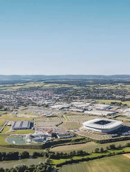 Luftaufnahme einer Stadt mit Stadion, Feldern und Gebäuden im Hintergrund.