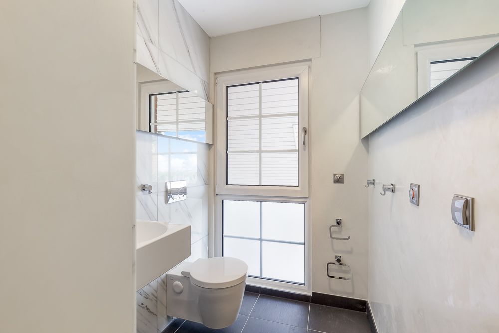 Modernes, helles Bad mit Wandtoilette, Waschbecken und Fenster mit Rollladen.