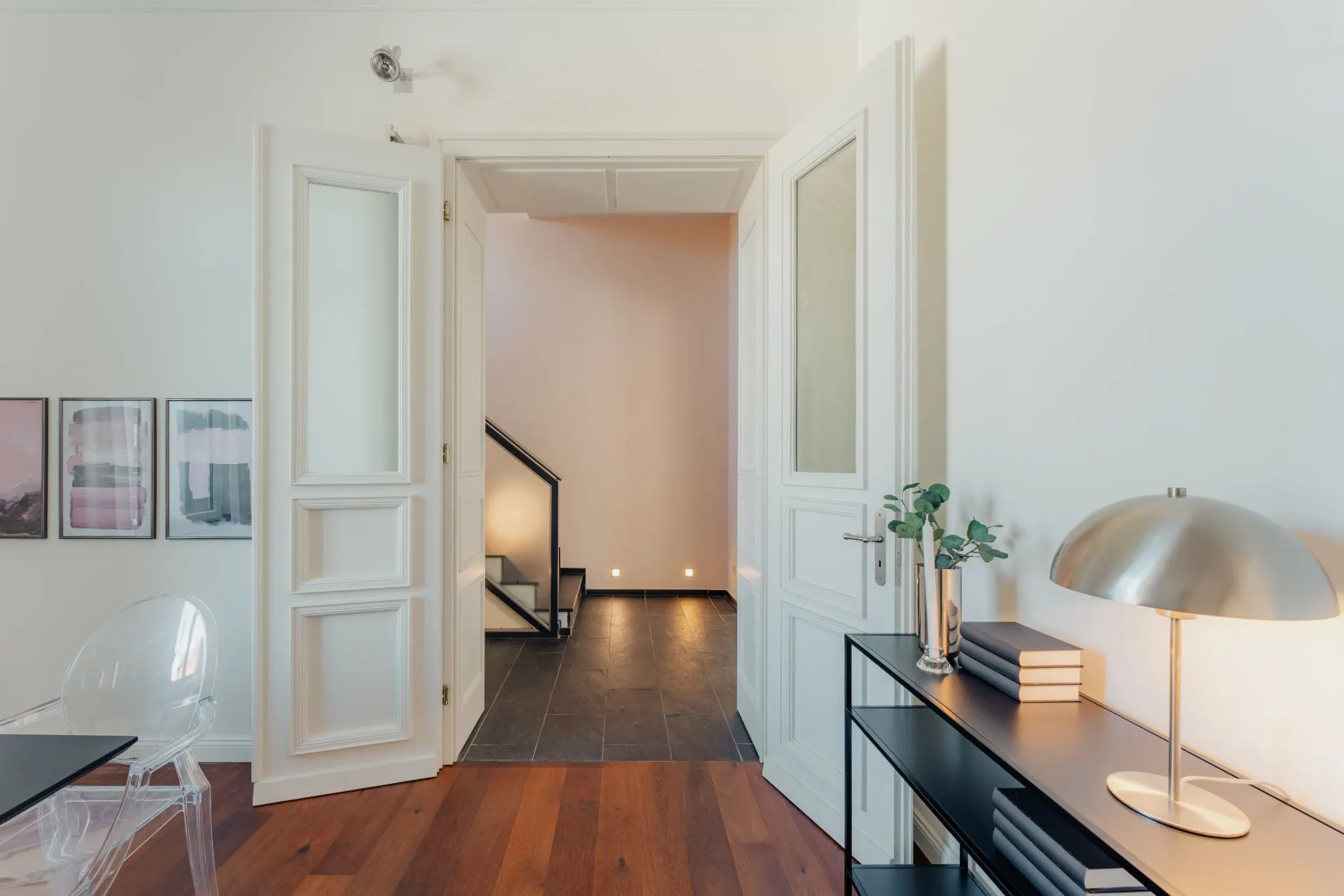 Helles Zimmer mit offenstehender Doppeltür, Blick auf Flur und Treppe, Schreibtisch mit Lampe und Pflanzen.