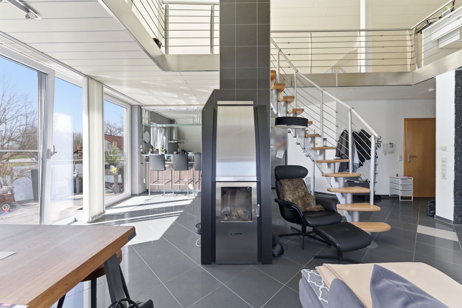 Modernes Wohnzimmer mit Kamin, Treppe, großen Fenstern und offener Küche.