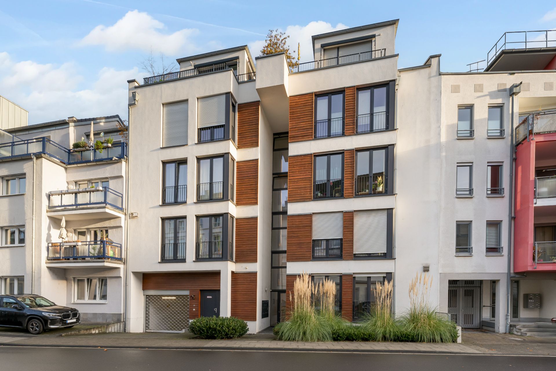 Modernes Wohnhaus mit großen Fenstern und Holzelementen, davor Ziergras und Straße.
