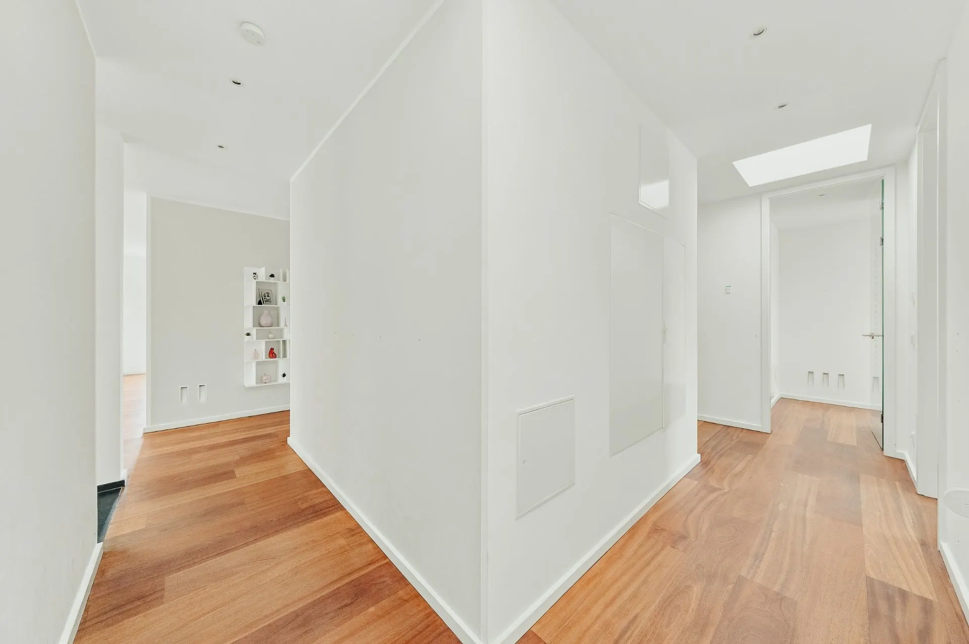 Heller Flur mit weißen Wänden und Holzboden, Regal im Hintergrund.