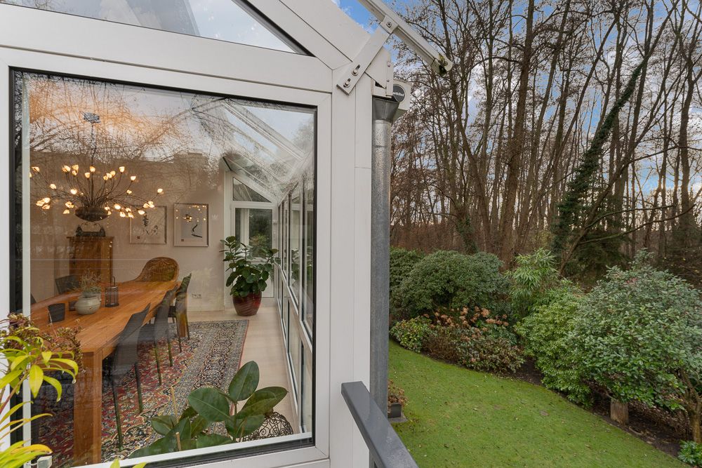 Blick durch Glasfenster auf Esszimmer mit Holztisch und Garten im Hintergrund.