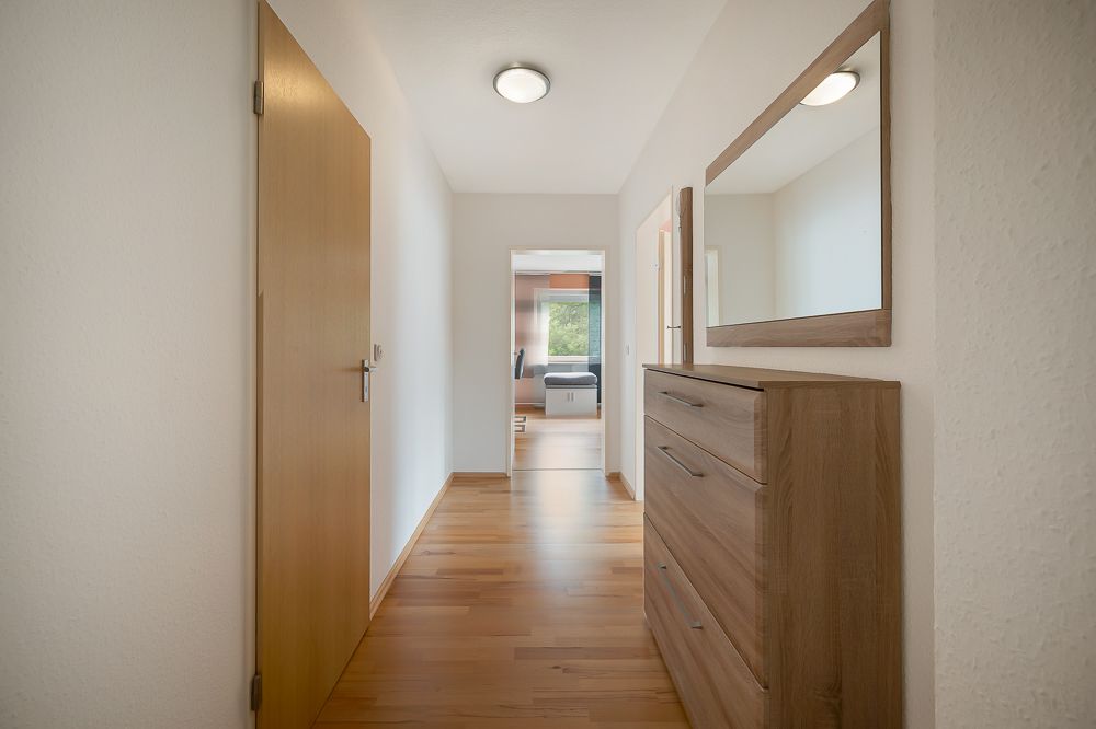 Heller Flur mit Holzkommode und Wandspiegel, Blick in einen weiteren Raum.