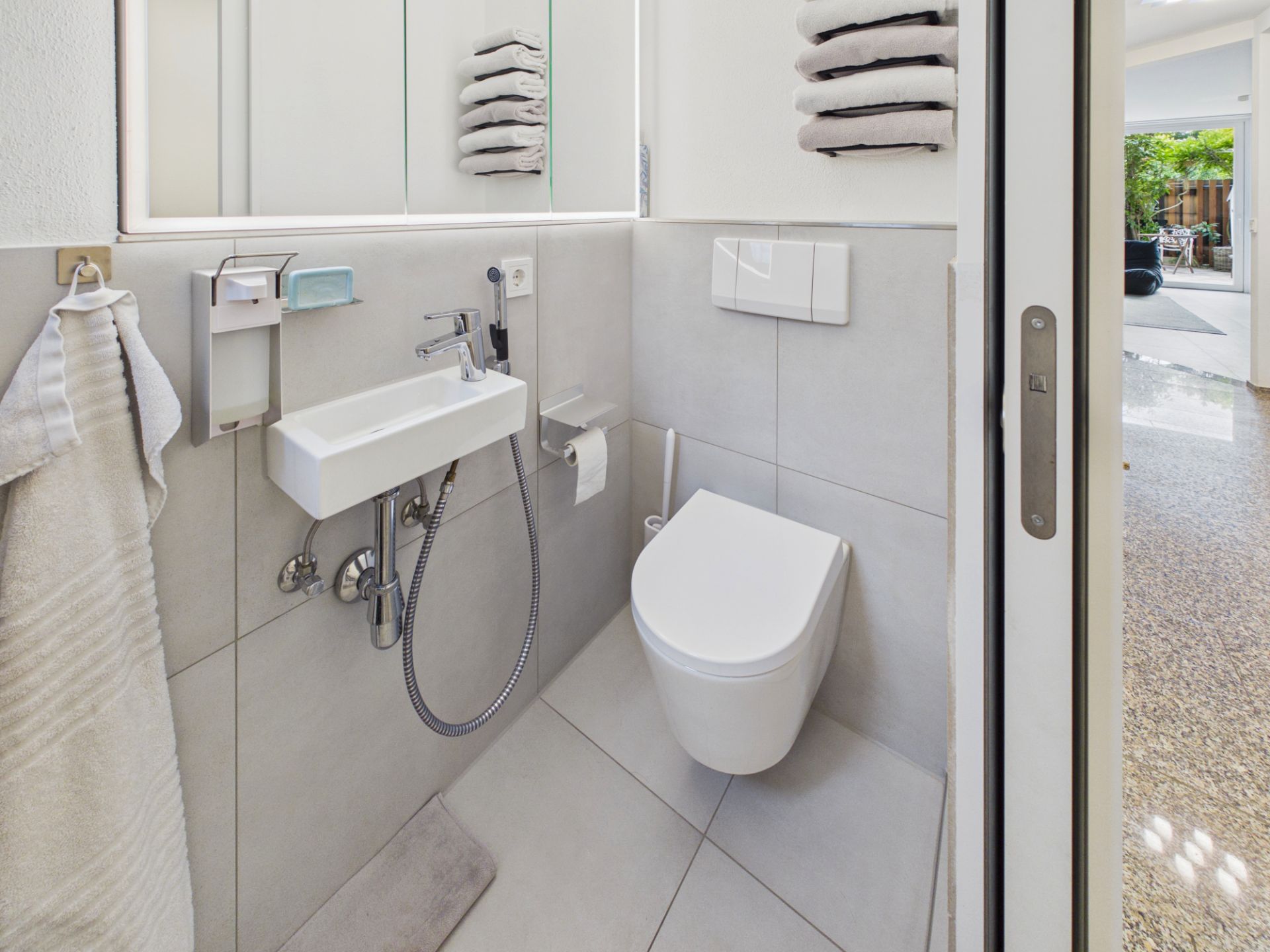Modernes, kleines Badezimmer mit Wandtoilette, Handwaschbecken und Spiegel.