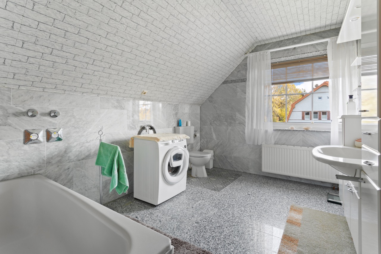 Helles Badezimmer mit Badewanne, Waschmaschine, Toilette und großem Fenster.