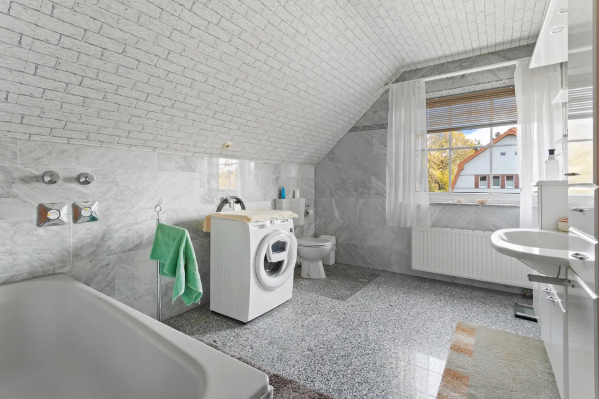 Helles Badezimmer mit Badewanne, Waschmaschine, Toilette und großem Fenster.
