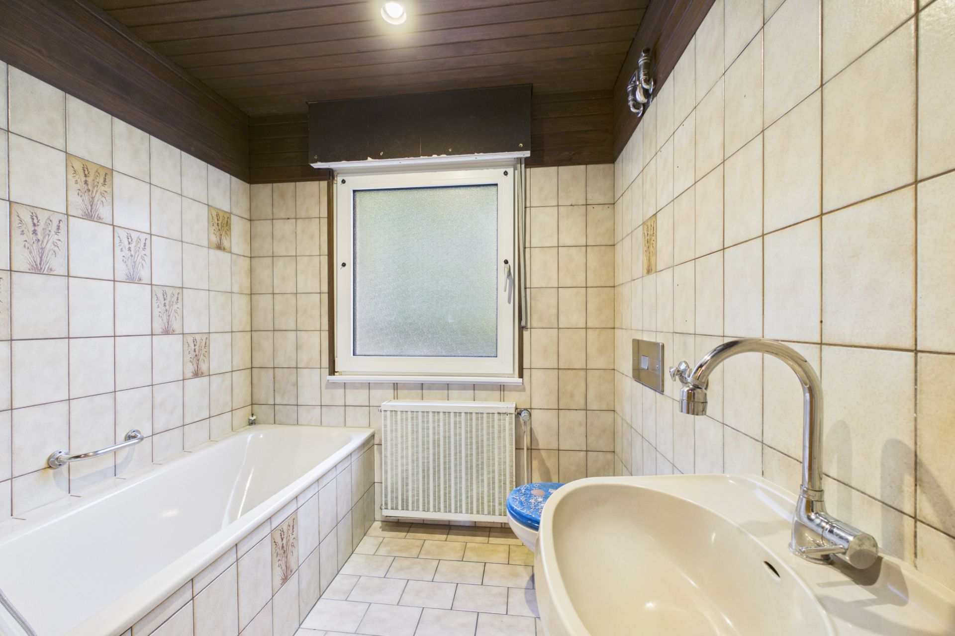 Badezimmer mit Badewanne, Waschbecken, Toilette und Fenster, gefliest mit hellen Fliesen.