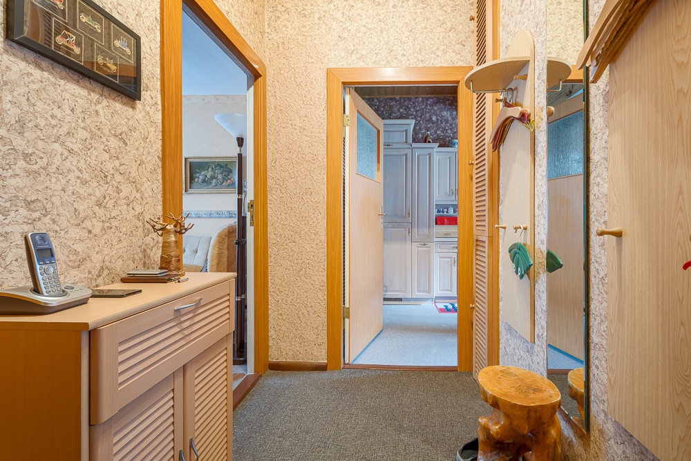Heller Flur mit Holzschränken, Spiegel und Blick in Wohnzimmer und Küche.