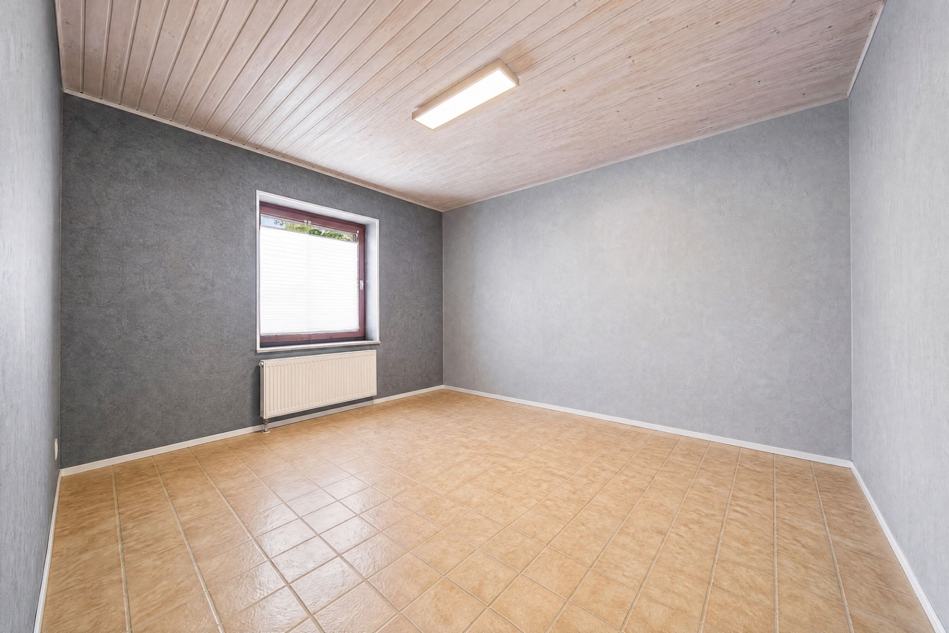 Leerer Raum mit grauen Wänden, Fliesenboden, Fenster und Deckenlampe.
