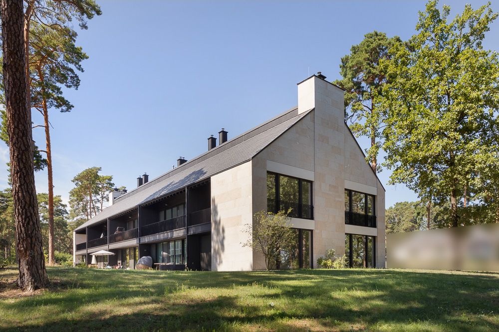 Modernes Wohngebäude mit großen Fenstern und Balkon, umgeben von Bäumen und Grünfläche.