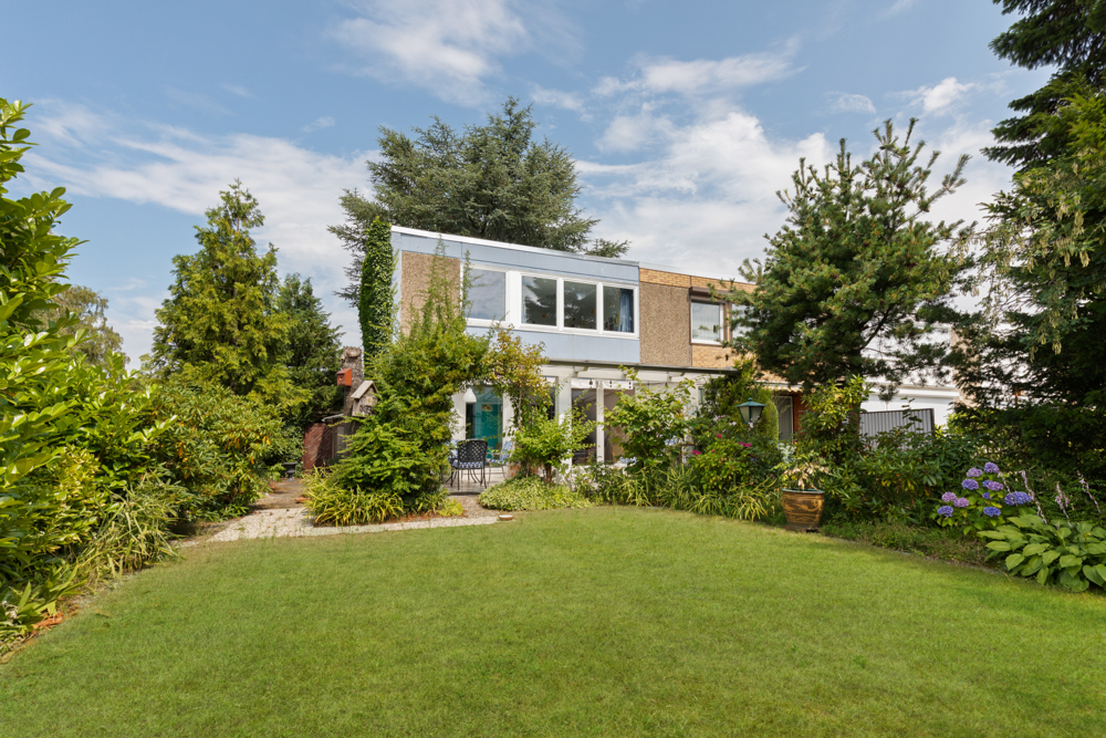 Zweistöckiges Wohnhaus mit großem Garten, umgeben von vielen Bäumen und Sträuchern.