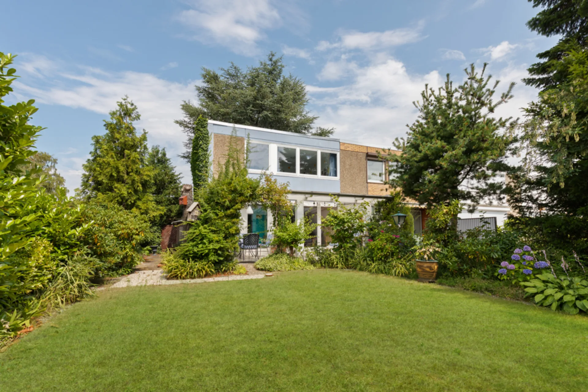 Zweistöckiges Wohnhaus mit großem Garten, umgeben von vielen Bäumen und Sträuchern.