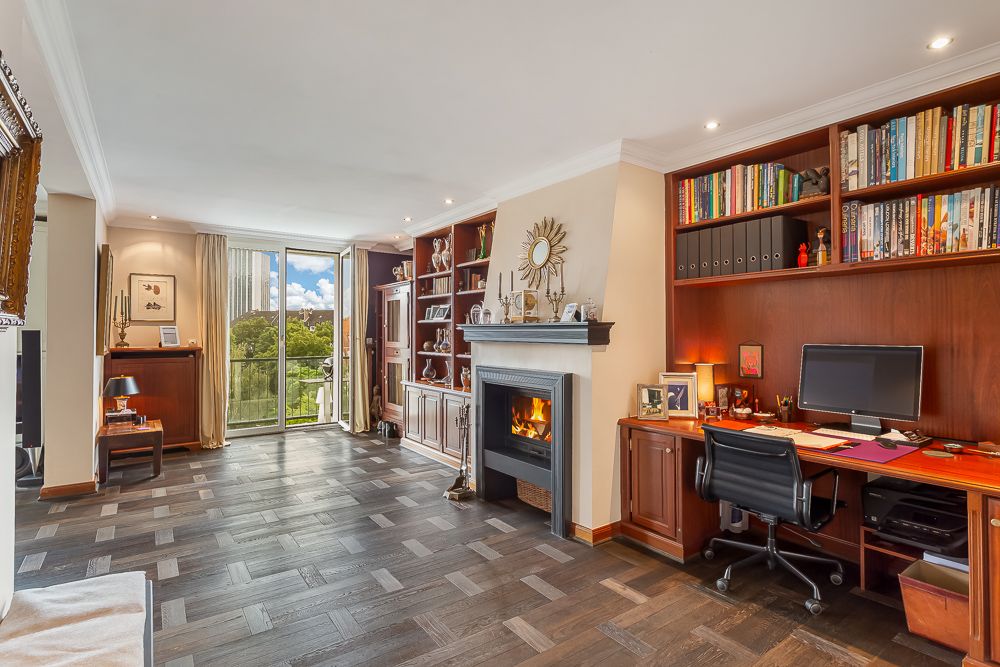 Wohnzimmer mit Kamin, großem Bücherregal, Schreibtisch und Glastür zum Balkon.