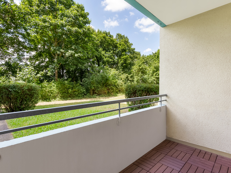 Balkon mit Holzfliesen und Blick auf eine grüne Gartenanlage mit Bäumen und Büschen.