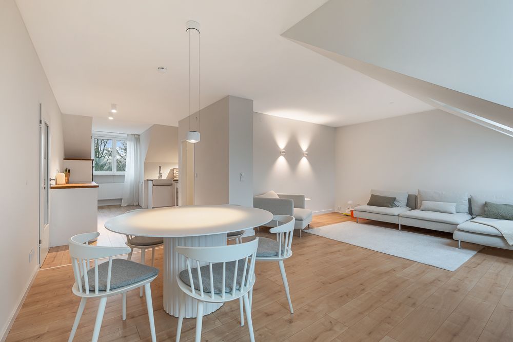 Helles Wohnzimmer mit Esstisch, Stühlen, Sofa und offener Küche auf Holzboden.