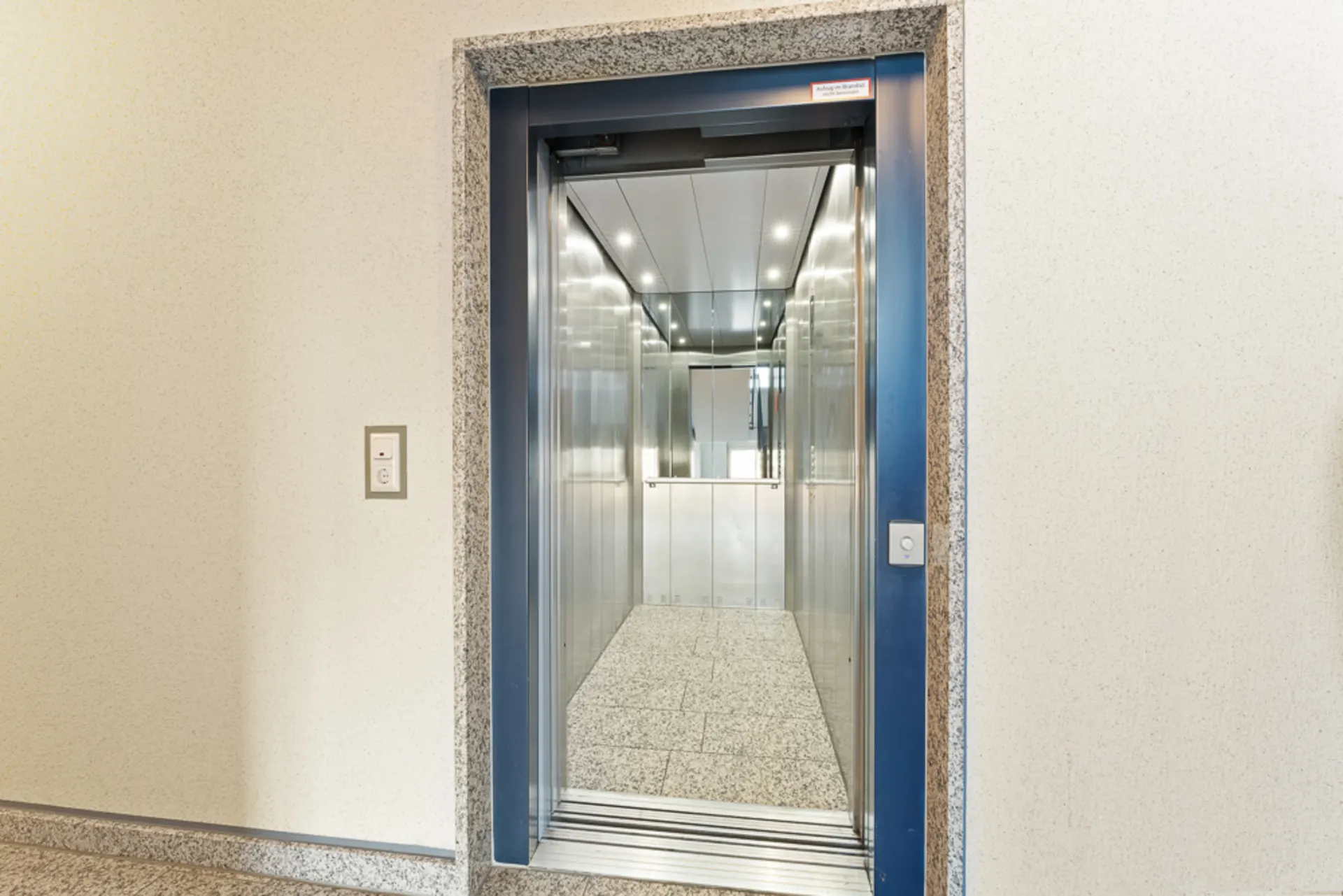 Offener Aufzug mit Edelstahlwänden und Granitboden in einem Wohngebäude.
