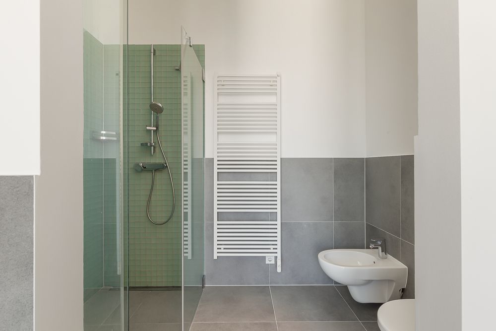 Modernes Bad mit Glasdusche, grün gefliest, Wandheizkörper und Wand-Bidet.