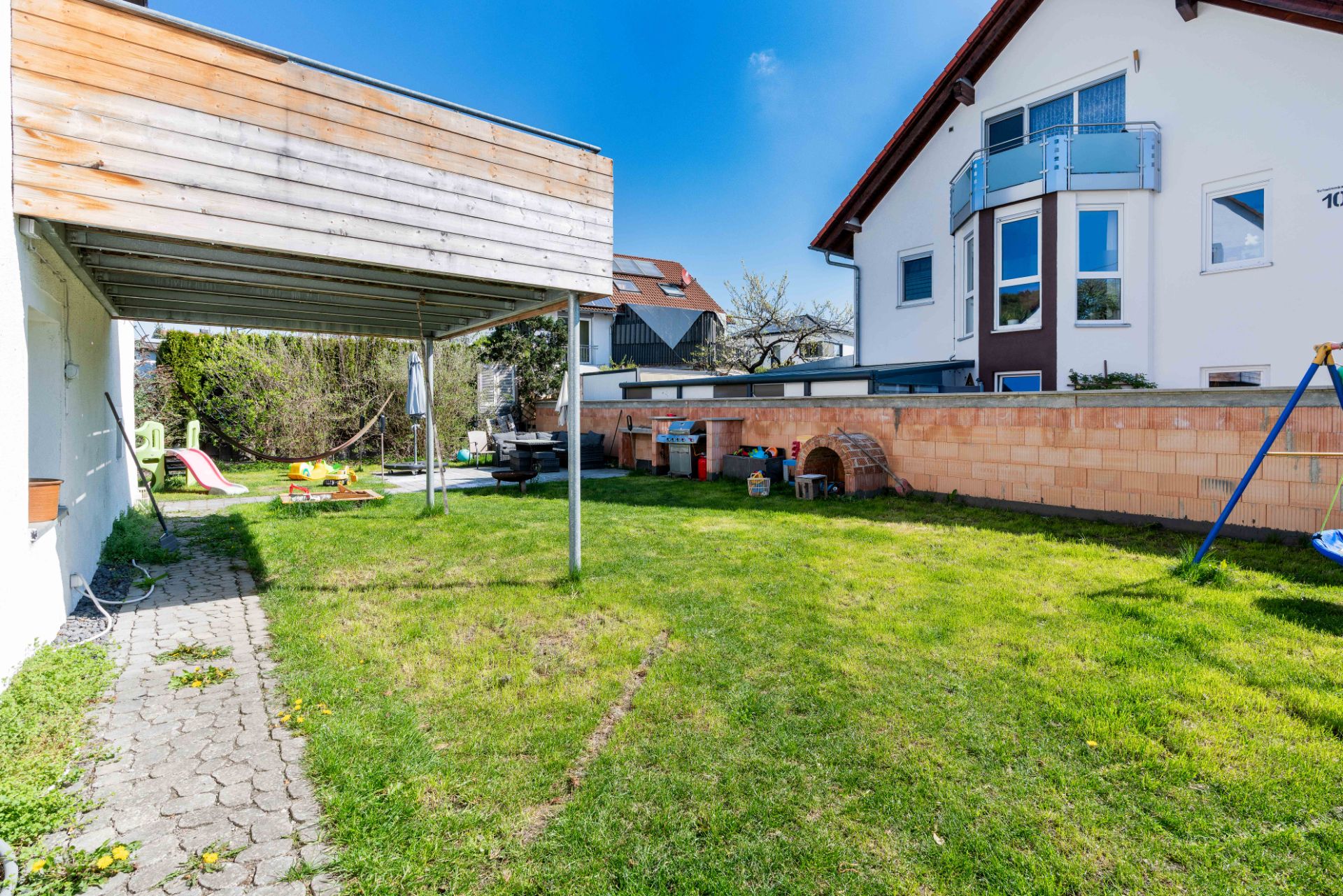 Garten mit Rasen, Kinderspielplatz und Terrasse neben einem Wohnhaus.