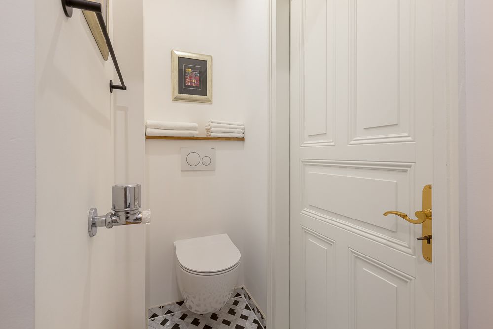 Kleines Badezimmer mit Wandtoilette, Handtüchern, Bild an der Wand und gemustertem Boden.
