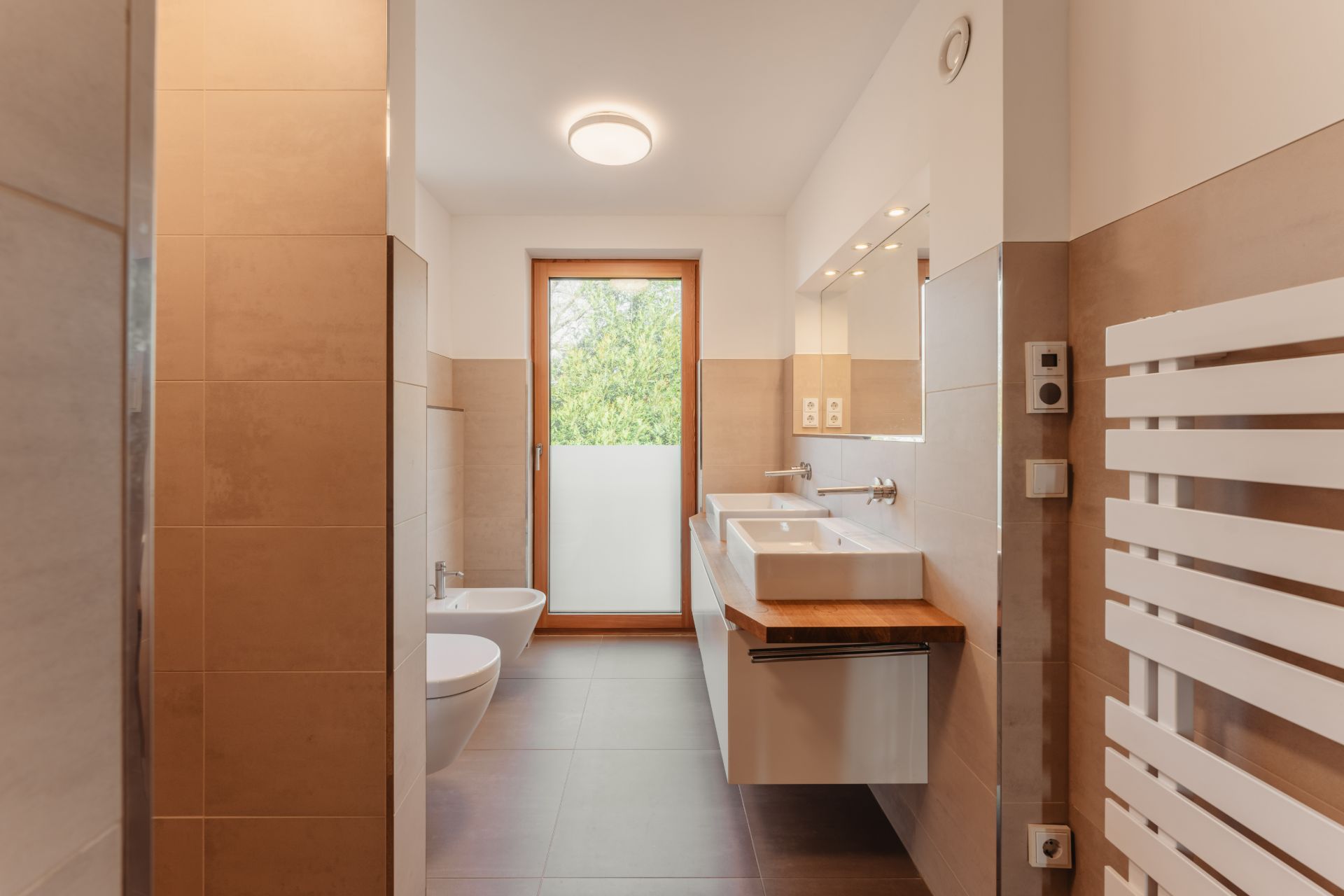 Modernes Badezimmer mit Doppelwaschbecken, Bidet, WC, großem Spiegel und Fenster.