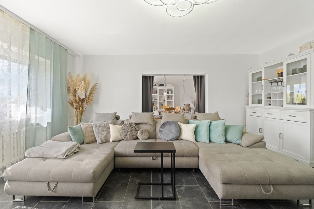 Modernes Wohnzimmer mit grauem Ecksofa, vielen Kissen und weißen Schränken.