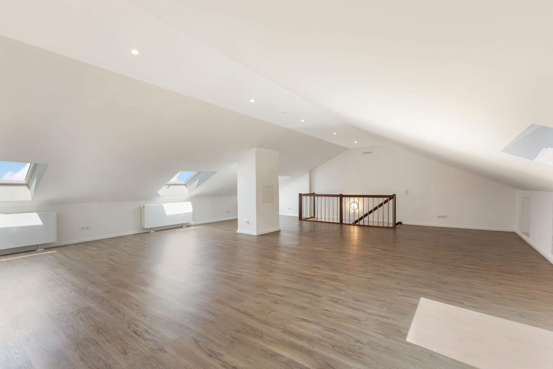 Großer, heller Dachgeschossraum mit Holzfußboden und mehreren Dachfenstern.