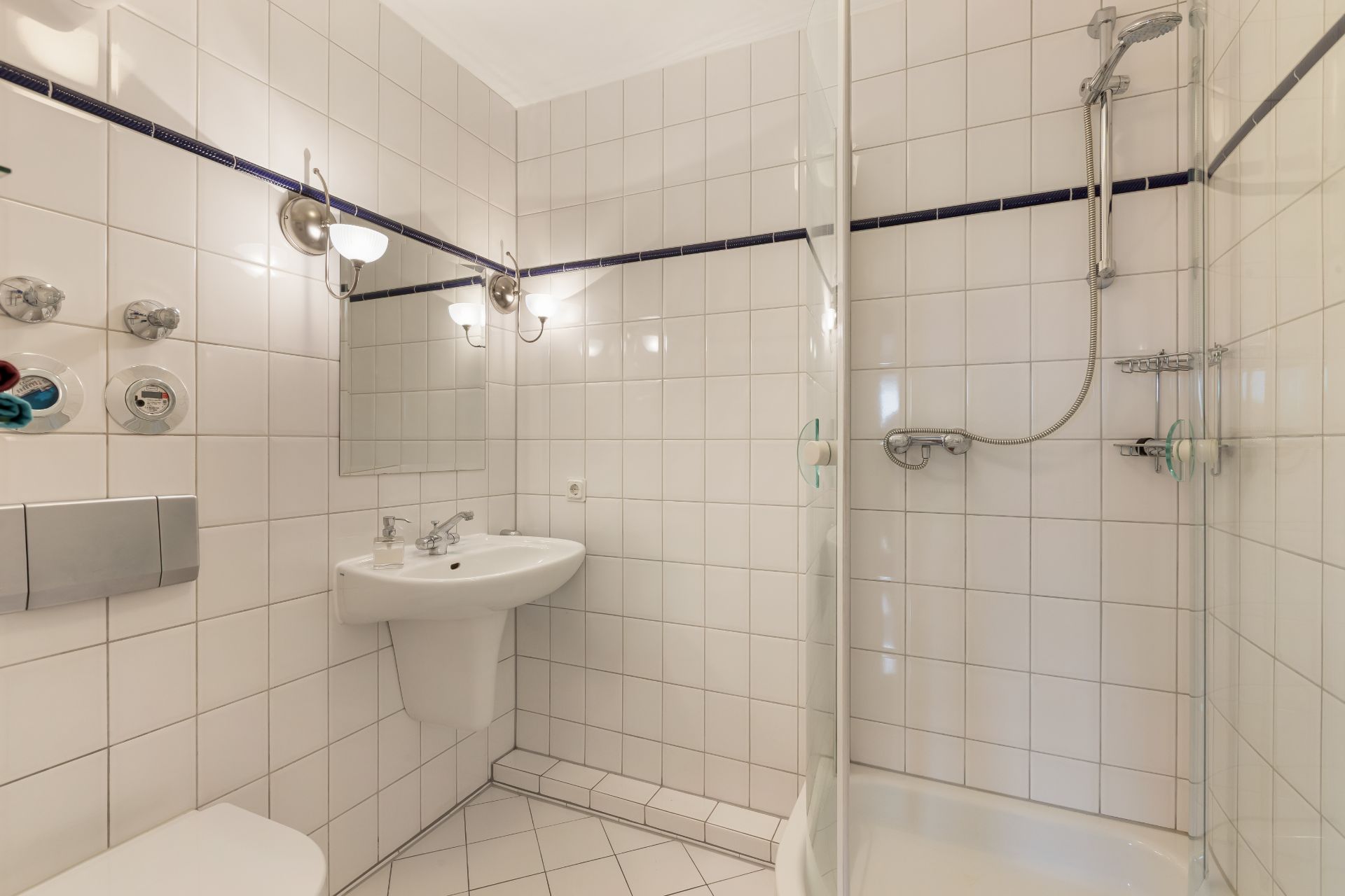 Helles Bad mit Duschkabine, Waschbecken, Spiegel, Hänge-WC und weißen Fliesen.