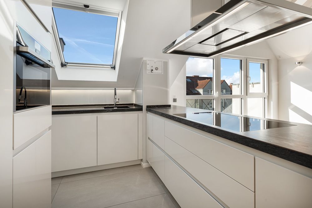 Moderne, helle Küche mit weißen Schränken, großem Fenster und Dachfenster.