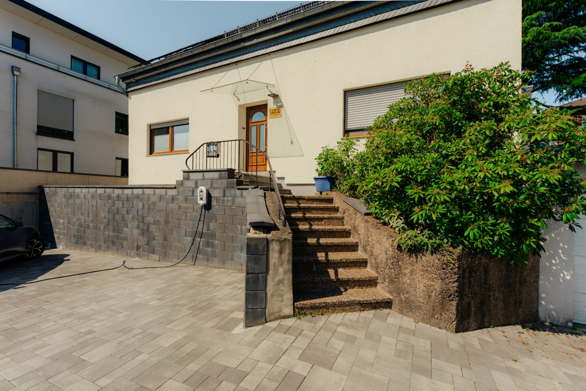 Außenansicht eines Hauses mit Treppe, Sträuchern und gepflastertem Hof.